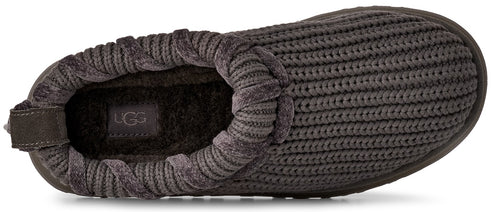 A top-down view of a dark grey, ribbed knit slip-on slipper with a plush, fuzzy interior and a visible UGG logo patch on the footbed.