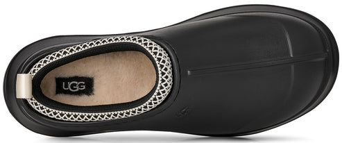 A top-down view of a black, slip-on rubber shoe featuring a light beige fleece insole with a black UGG logo tag and a white woven mesh collar trim.