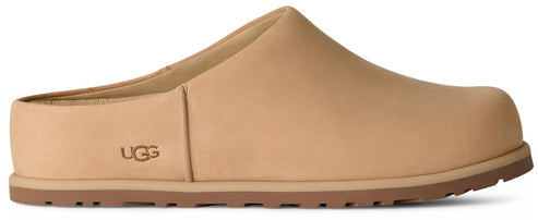 A tan slip-on shoe with a rounded toe, a flat sole with a brown tread, and the brand name UGG embossed on the side.