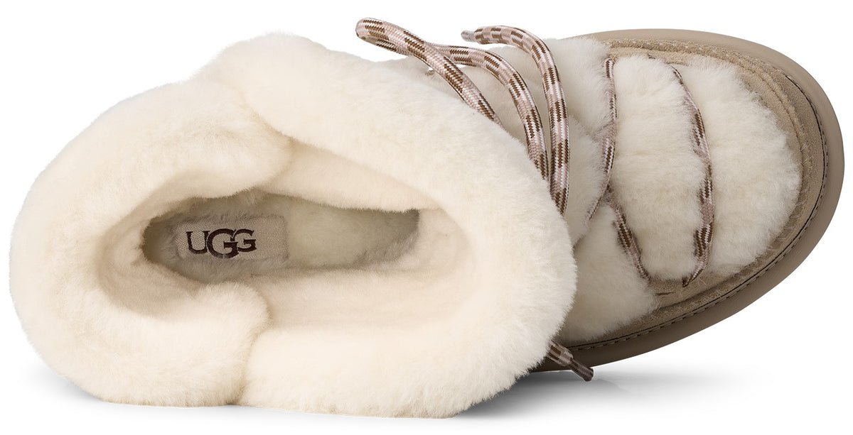 A top-down view of a cream-colored, fluffy, shearling-lined winter boot with crisscross lace-up details and the text UGG visible on the insole.
