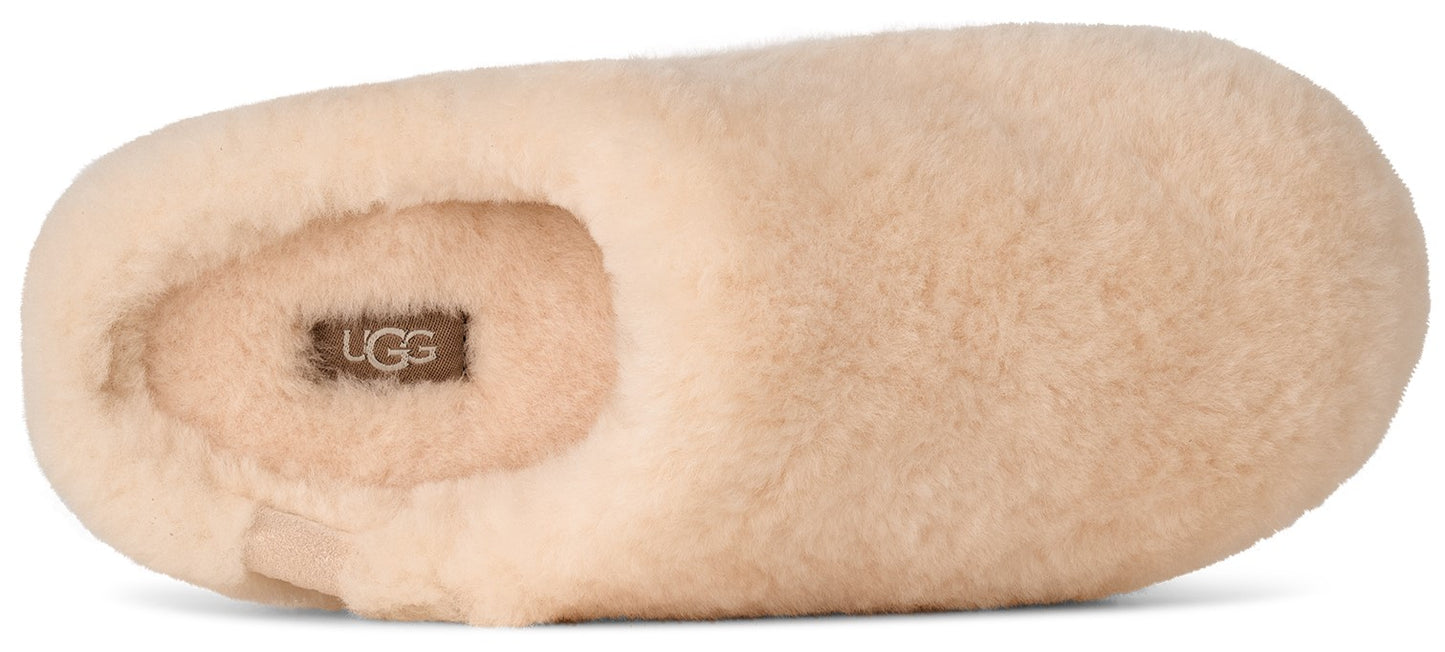 A beige, fluffy sheepskin slipper viewed from above, featuring an UGG logo label on the insole.