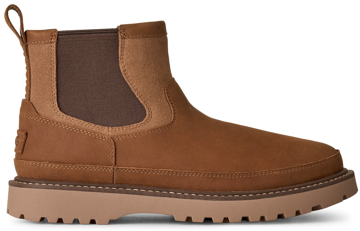 A brown leather Chelsea boot with a thick lug sole and a matching brown elastic side panel, featuring a pull tab at the heel and a small embossed logo on the rear.