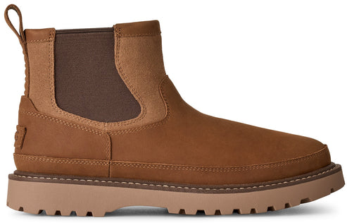 A brown leather Chelsea boot with a thick lug sole and a matching brown elastic side panel, featuring a pull tab at the heel and a small embossed logo on the rear.