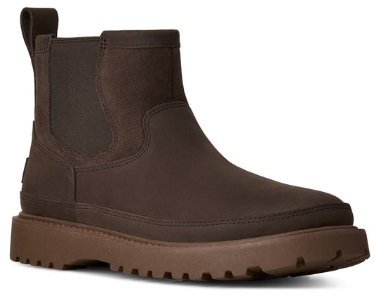 A dark brown Chelsea boot with a pull tab at the back, featuring a matte leather upper, matching elastic side panels, and a chunky, lugged brown rubber sole.