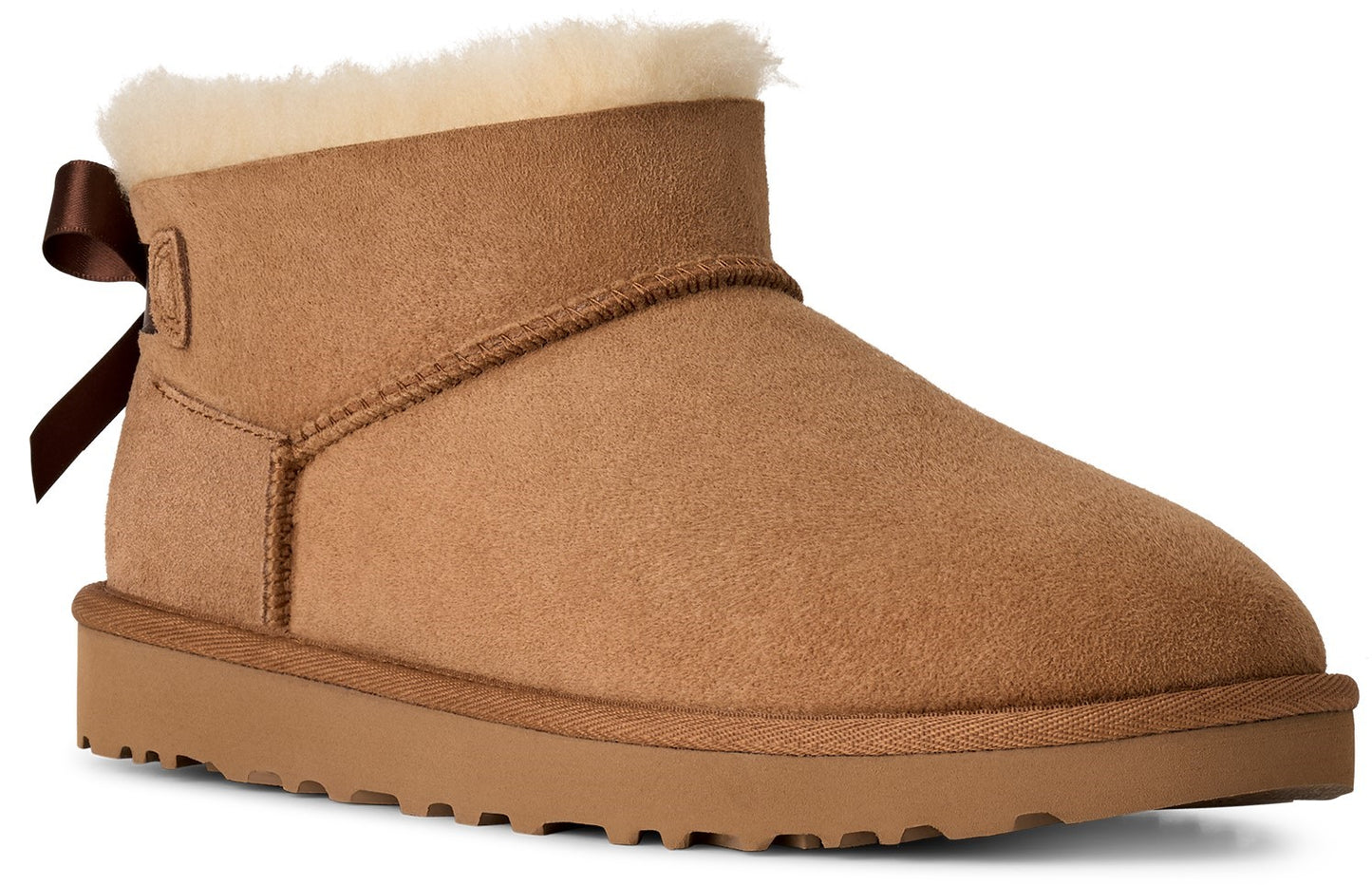 A tan suede ankle boot with a beige shearling lining at the cuff and a small brown ribbon bow attached at the back heel.
