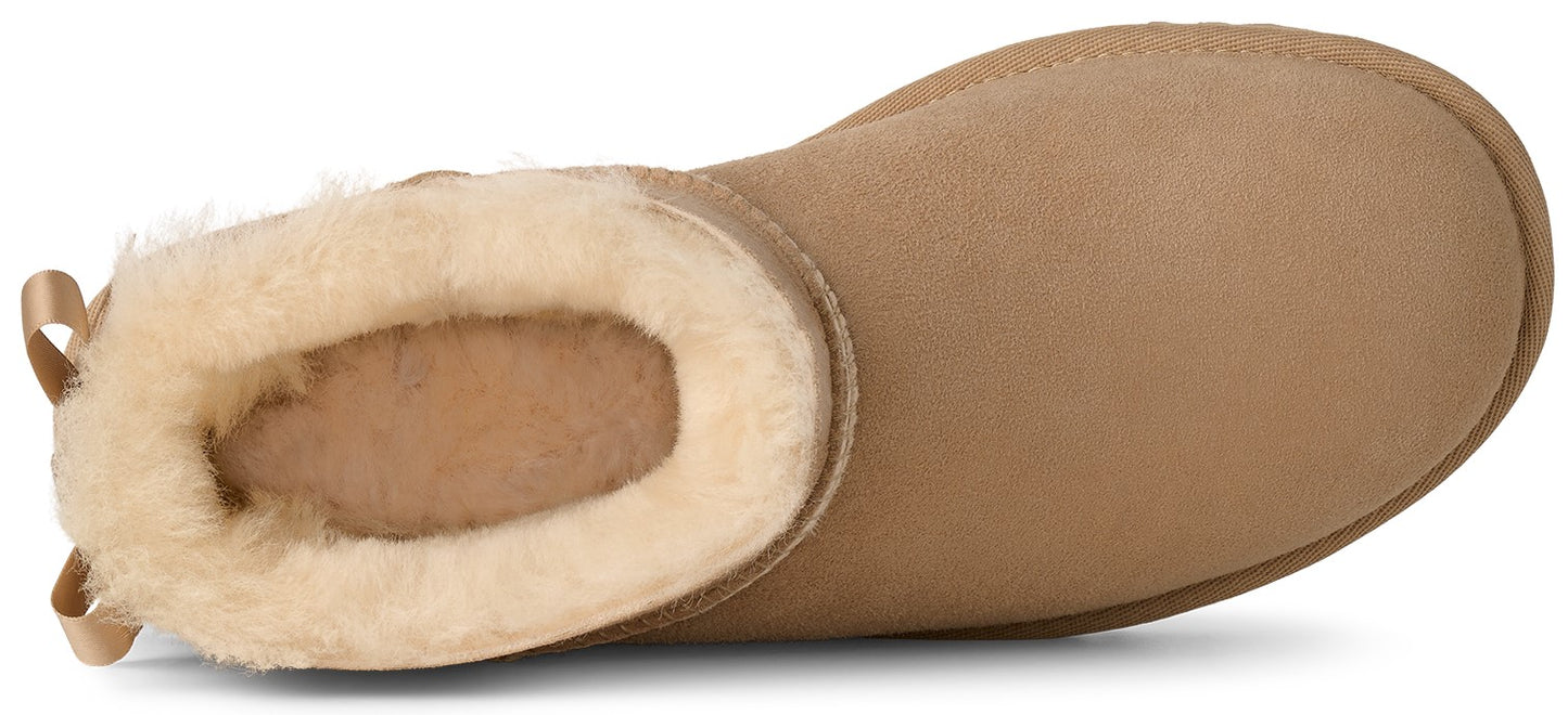 A tan suede slip-on ankle boot viewed from above, featuring a plush cream-colored faux fur lining and a small tan ribbon pull tab on the heel.