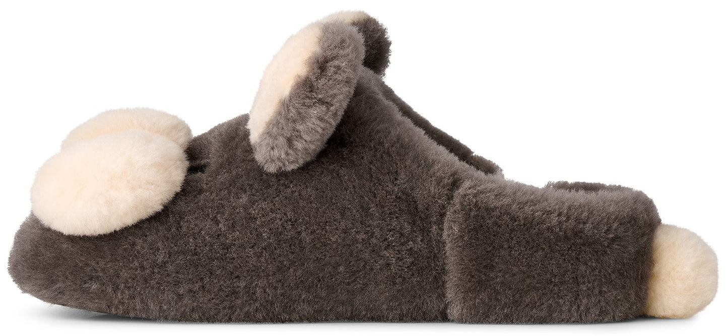 A fuzzy, dark grey sheepskin slipper featuring decorative, cream-colored, rounded ear-like patches on the top and a small cream-colored tail-like detail at the back heel.