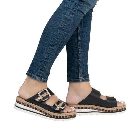 Person wearing blue jeans and black double buckle sandals with white soles.