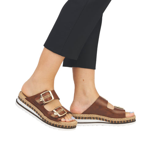 A pair of brown slide sandals with gold buckles and white soles.