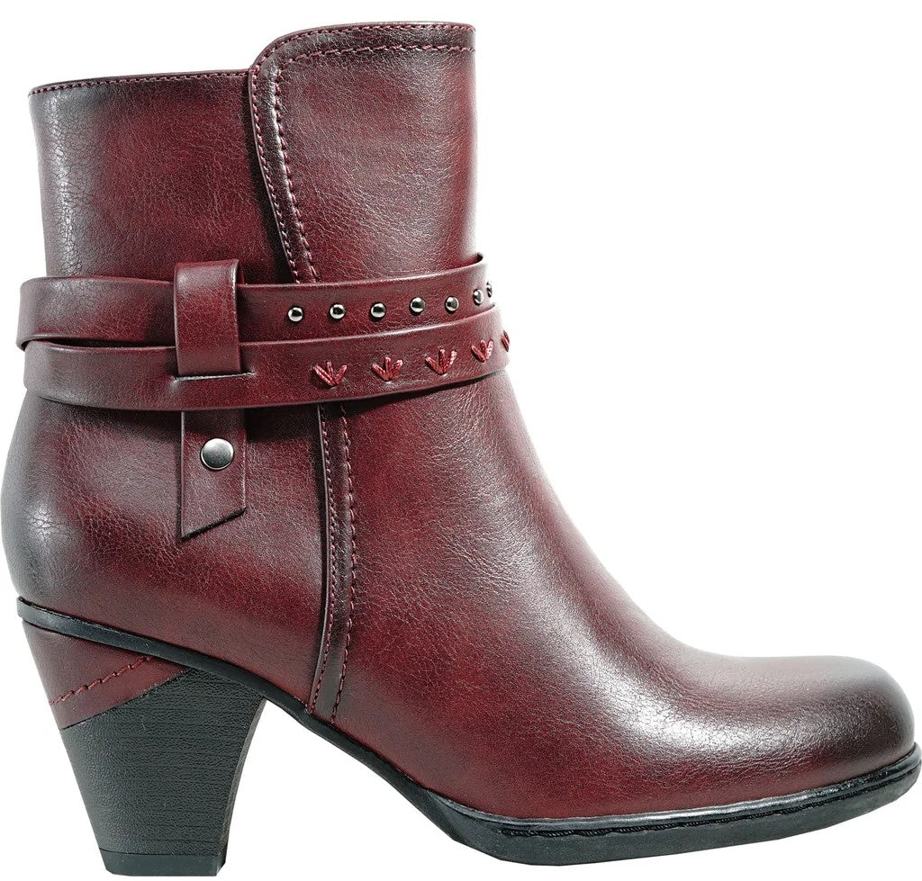 A maroon, block-heeled ankle boot featuring an adjustable strap with decorative metal studs and stitched heart accents, designed with a rounded toe and a dark synthetic textured finish.