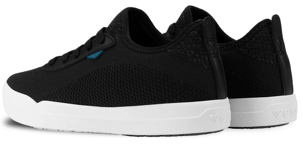 A pair of black knit sneakers with a low-profile design, white rubber outsoles, and a small blue accent tab on the side.