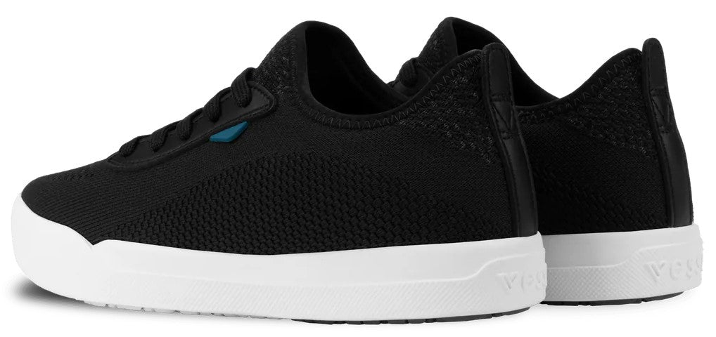 A pair of black knit sneakers with white soles, viewed from a side-angle, featuring a subtle blue accent near the laces and a minimalist design.