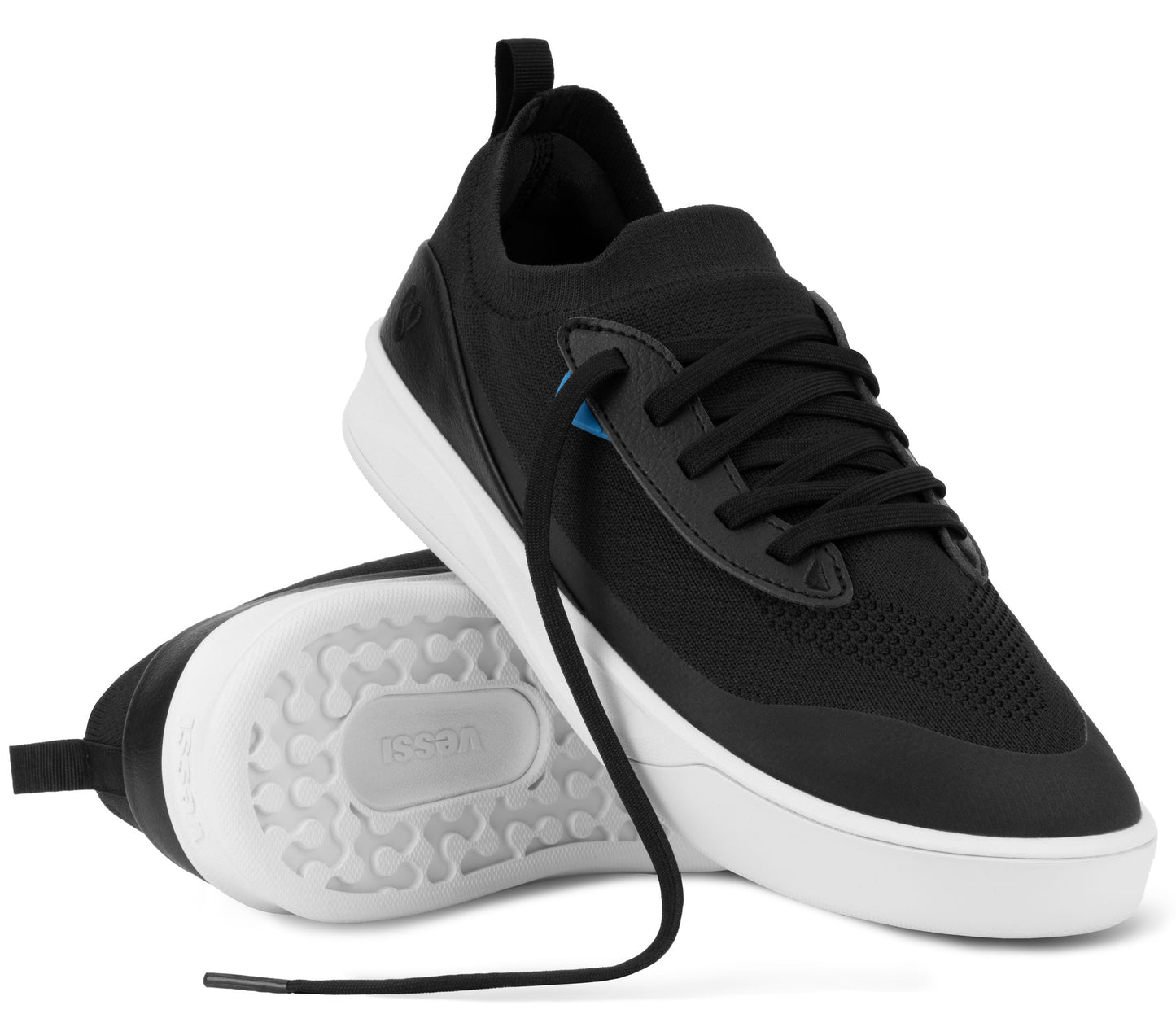 A pair of black low-top sneakers with white soles, one shown from the side and the other showing the white tread pattern on the bottom, featuring black laces and subtle blue accents on the eyelets.
