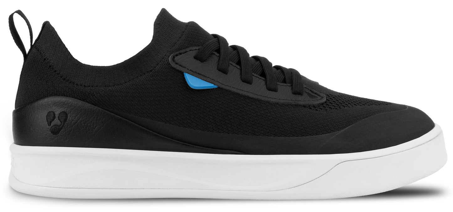 A black low-top sneaker with a white rubber midsole, a pull tab on the heel, and a small blue accent piece near the laces.