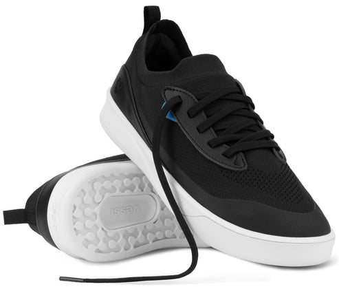 A pair of black and white athletic sneakers, with one shoe upright and the other lying on its side showing the patterned white rubber outsole with the word 'leessi' embossed in the center.