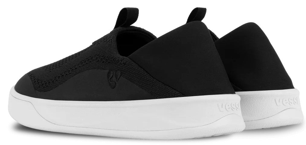 A pair of black slip-on sneakers with white soles, viewed from the rear three-quarter angle.
