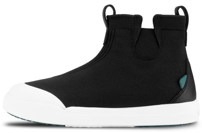A black slip-on ankle boot with a high-top design, featuring a white rubber cap toe and matching white flat sole, with pull tabs on the collar and a small teal accent tag on the heel.