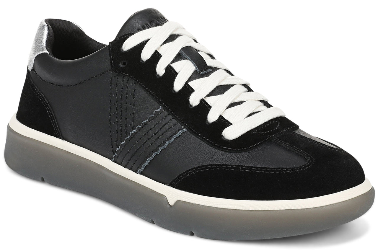 A low-top sneaker in black leather and suede, featuring a white lace-up closure, a silver heel accent, and a chunky translucent grey rubber outsole with a white midsole.