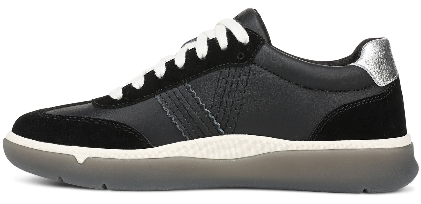 A black leather sneaker with black suede overlays at the toe and heel, white laces, a silver metallic detail on the heel tab, a thick off-white midsole, and a translucent grey rubber outsole.