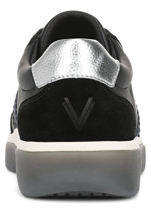 A rear-view close-up of a black sneaker featuring a metallic silver heel tab, a black suede heel panel with a prominent V-shaped logo, and a thick, semi-translucent grey rubber sole.