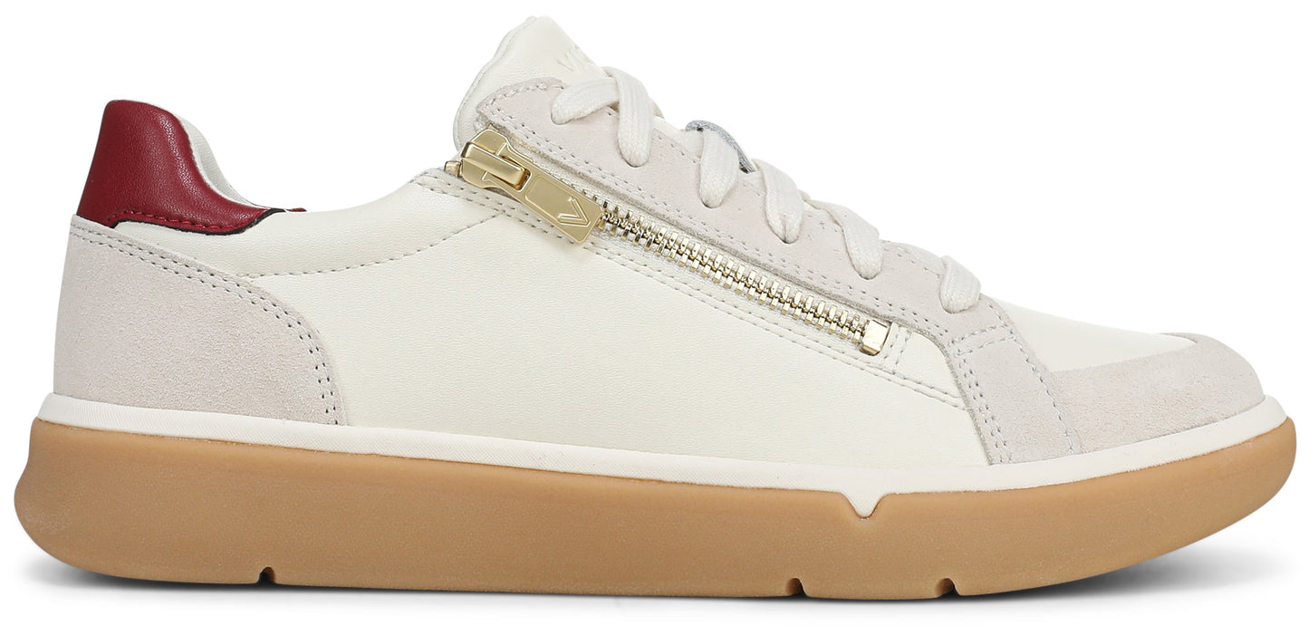 A low-top sneaker featuring an off-white leather and suede upper, a gold-toned zipper detail running along the side, a maroon heel tab, and a solid tan rubber sole.