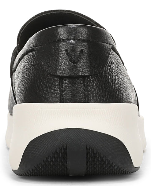 A close-up view of the back heel of a black textured leather slip-on shoe, featuring a thick, white cushioned midsole and a black, treaded rubber outsole with a subtle brand logo embossed on the leather heel counter.