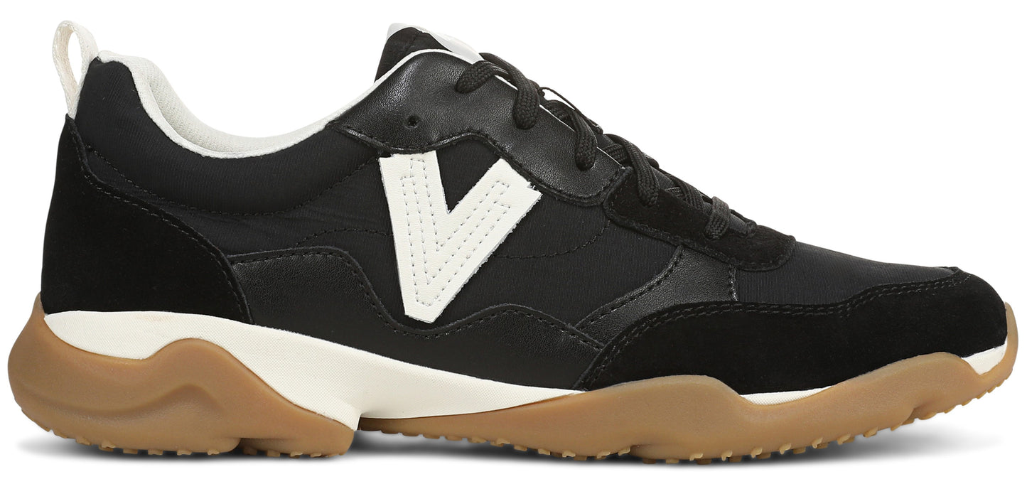 A low-top sneaker featuring a black upper with a prominent white V-shaped logo on the side, a white midsole, and a thick, textured gum-colored rubber outsole.