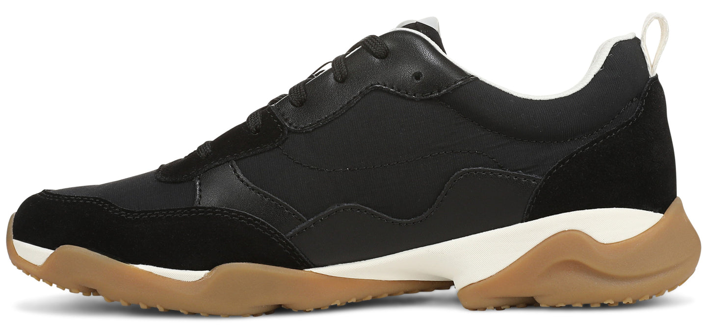 A side view of a black athletic sneaker with a white midsole and a brown gum rubber outsole.