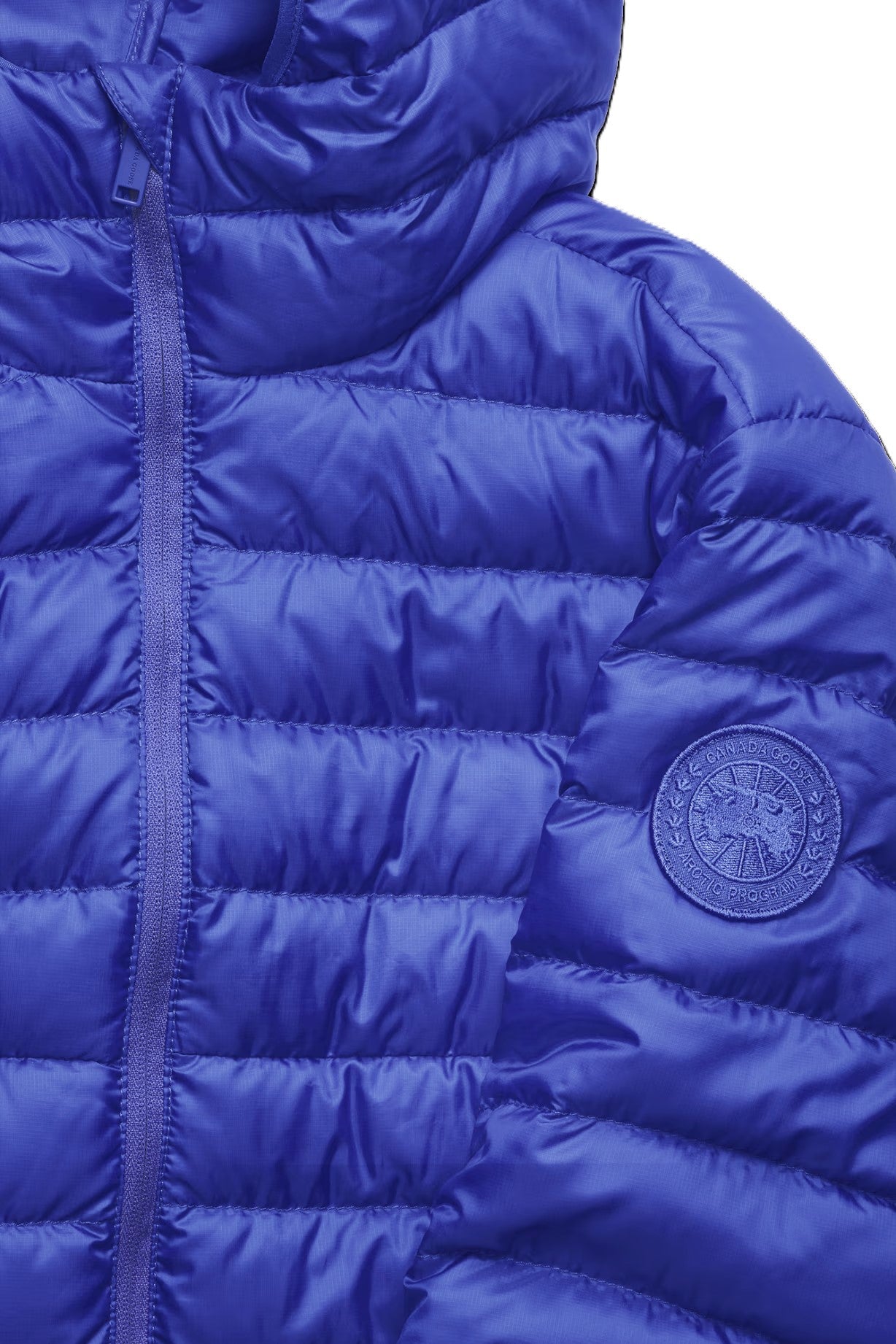 Close up of a blue hooded puffer jacket with a front zipper and a round logo patch on the right arm.