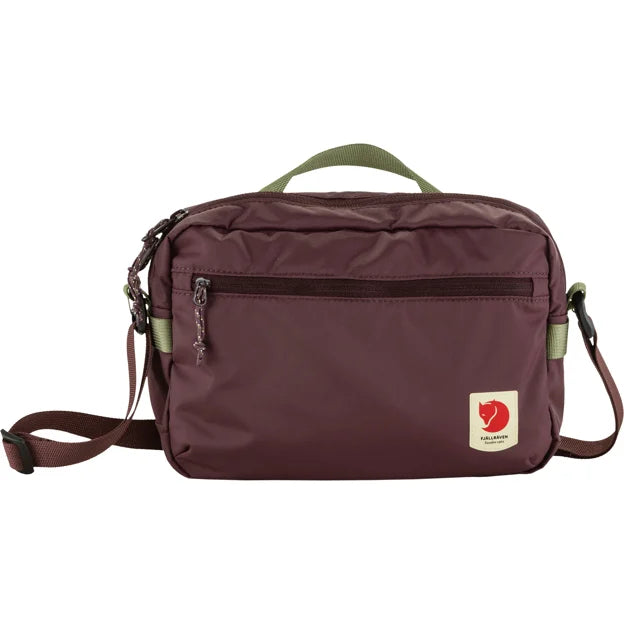Maroon messenger bag with a front pocket, a green top handle, and a logo patch.
