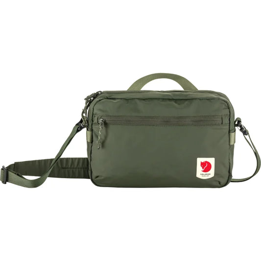 Front view of a solid green rectangular bag with a top handle, an adjustable shoulder strap, and a small square tag with a red and white logo on the bottom right.