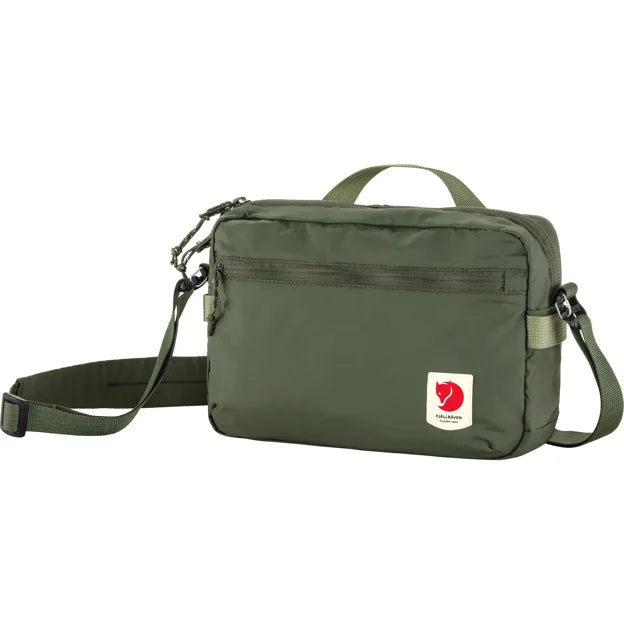 Olive-green crossbody bag with adjustable shoulder strap, top handle, zippered top closure, front zippered pocket, and red logo.