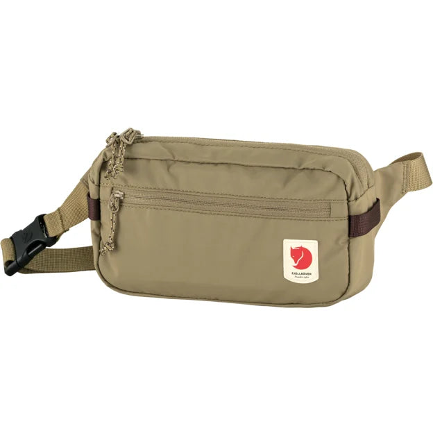 A khaki-colored fanny pack featuring an adjustable clip strap, zipper closures, and a red and white circle brand patch.