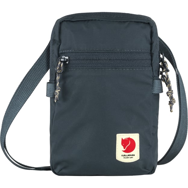 Close-up of a small dark blue Fjallraven crossbody bag, showing the front zip pocket, logo, and the adjustable strap.