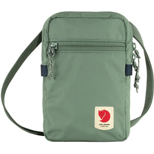 Small, rectangular, green crossbody bag with zipper at top and logo with red circle and white image on the lower right.