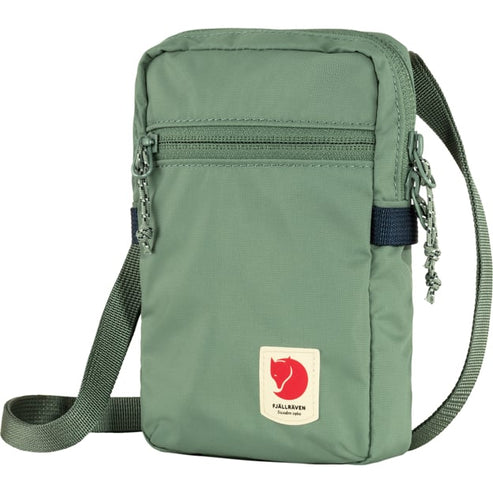 Small, vertical, green bag with a zipper and a shoulder strap, featuring a small, rectangular logo with a red arctic fox.