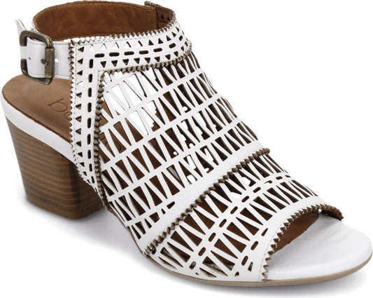 A white sandal with a medium block heel and an ankle buckle closure; the upper is intricately cut.