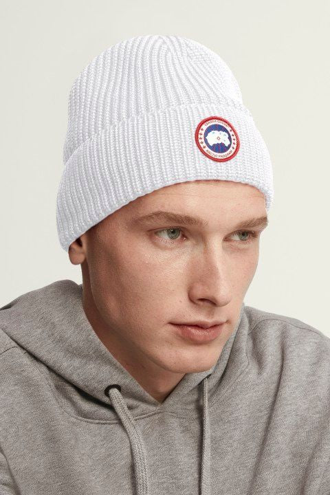 Man wearing a white knitted beanie with a circular badge.