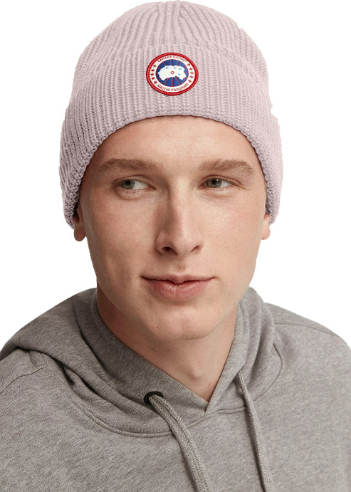 Man wearing a light pink ribbed beanie with a circular emblem.
