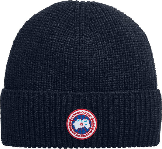 Navy blue knit beanie with round badge featuring a world map and text 'CANADA GOOSE ARCTIC PROGRAM'.