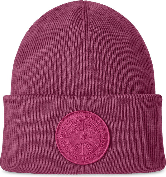 Close-up of a magenta knit beanie with a circular logo near the brim.