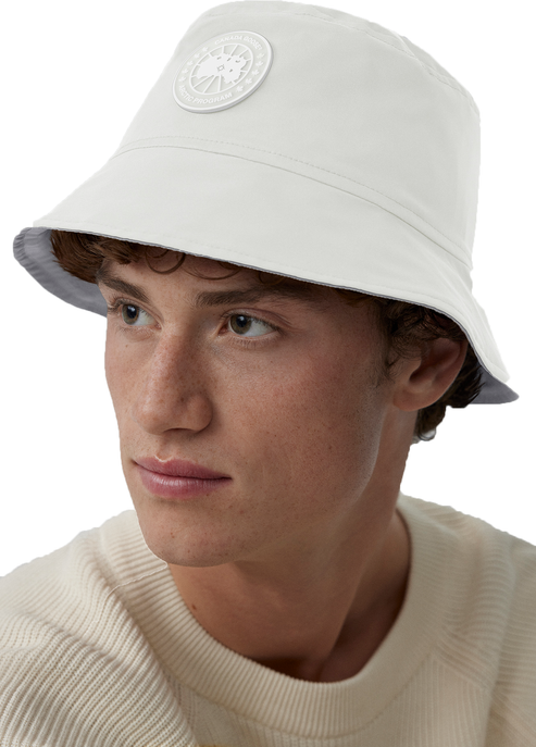 Person wearing a white bucket hat with a round, white logo patch.