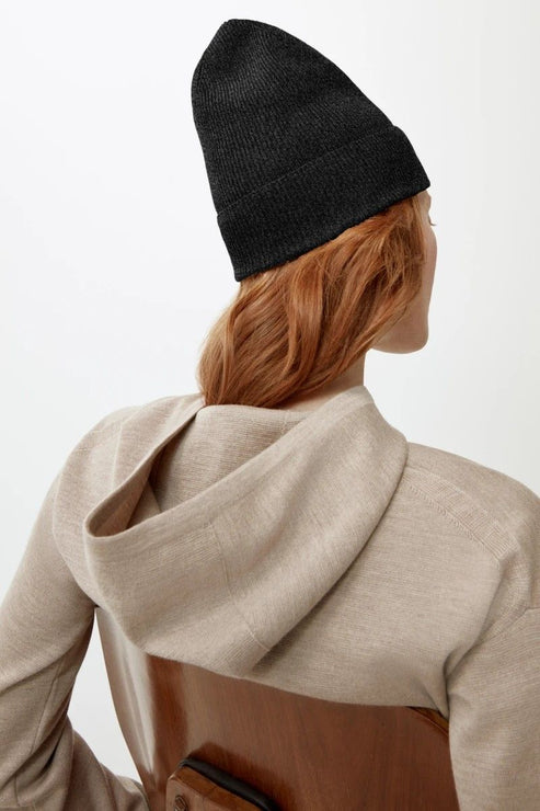 Person with red hair wearing a black beanie and beige hooded jacket.