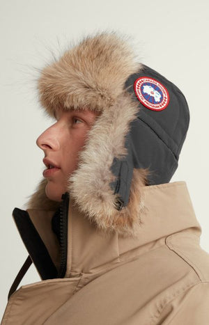 Person wearing fur-trimmed winter hat with circular logo on side.