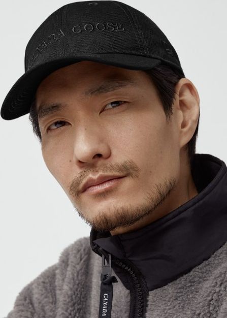 Man wearing a black cap with CANADA GOOSE on it and a black and gray fleece jacket.