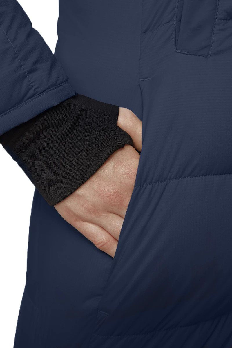A close-up of a person's hand reaching into the pocket of a dark blue puffer jacket with a black cuff visible.