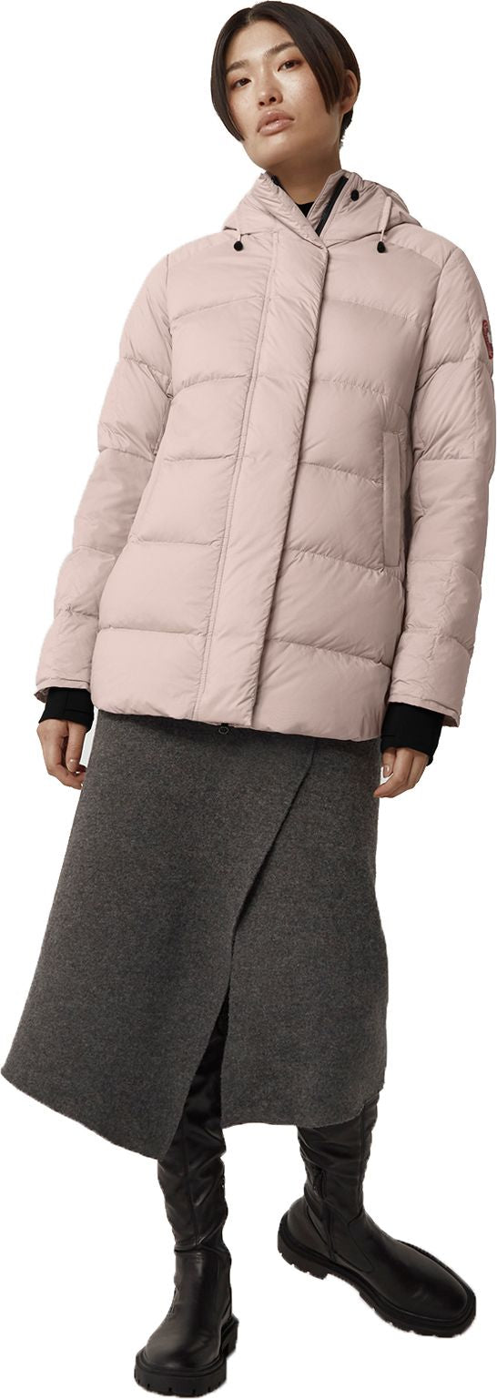 A woman wearing a light pink puffer jacket, a gray skirt, and black boots.