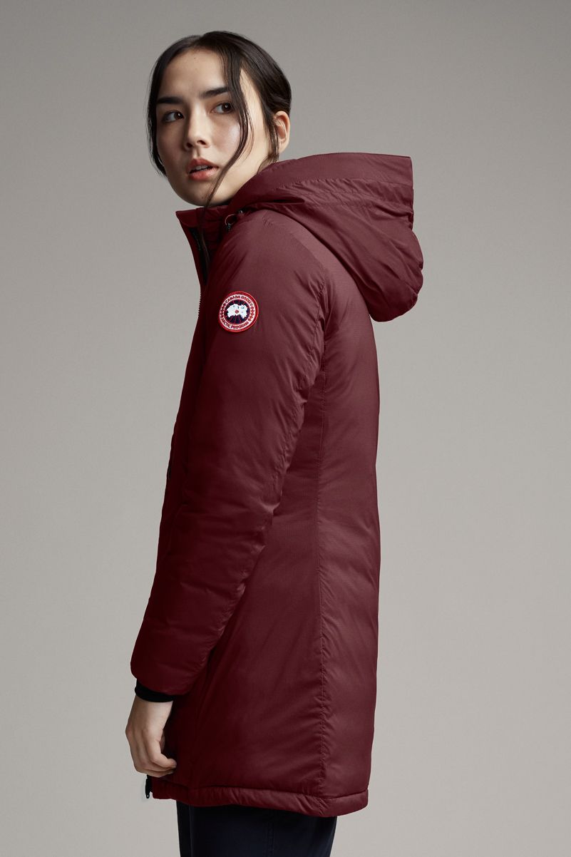Woman in long, maroon hooded jacket with circular emblem on sleeve.