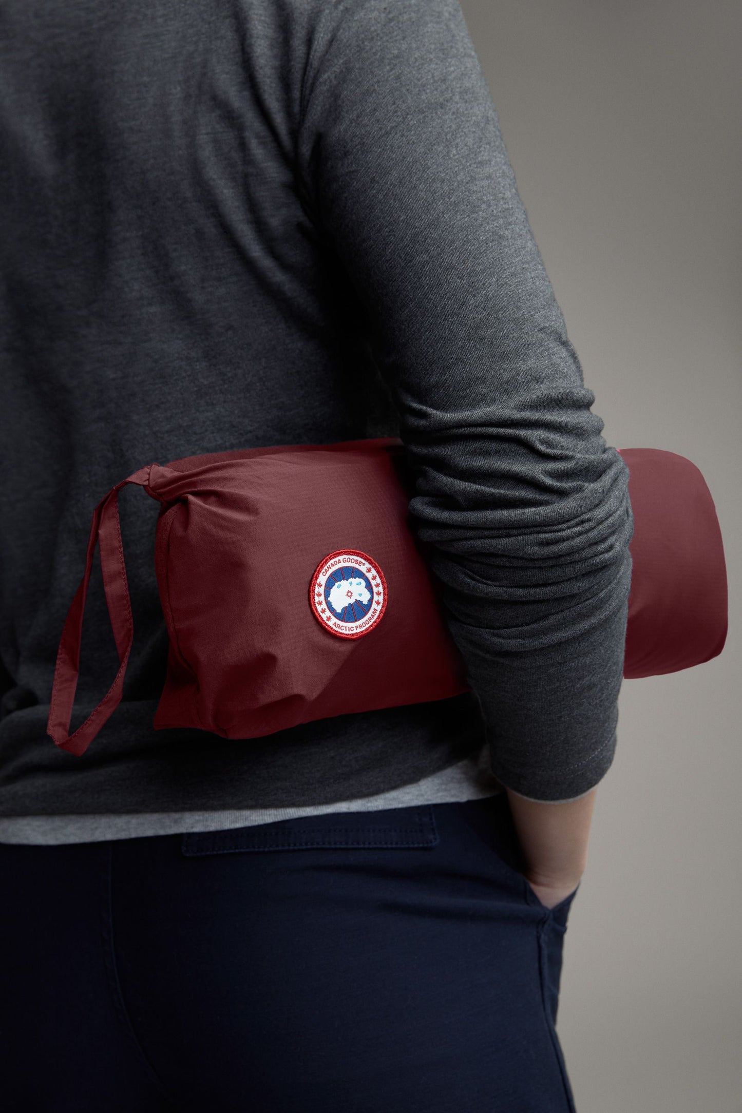 Rolled-up maroon jacket with circular Canada Goose emblem held at waist.