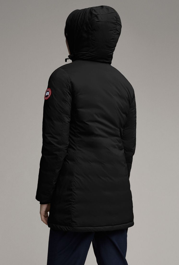A person is seen from the rear wearing a long, black hooded jacket with a circular red, white, and blue logo on the left sleeve.